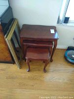 Three wooden vintage nesting tables stacked together on wood floor with two mirrors beside them.