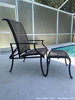 Side view of the patio chair and footstool set by a pool. Shows black metal frame and mesh fabric material. Ambient outdoor lighting.
