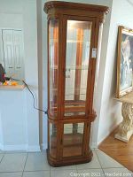 Front view of the curio cabinet showing wooden frame and glass doors with lighting on inside.