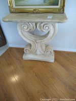 Oblique front view of plaster console table showing scroll design and top surface with stain