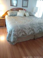 Full view of king size bed made with reversible quilt featuring large damask floral pattern in soft tones, with matching pillows and dust ruffle on wooden floor.