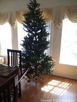 7-foot artificial Christmas tree standing assembled in room by windows, showing full tree height and branch detail.
