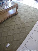 Full view of sage green area rug under a glass-topped coffee table showing sculpted square textured pattern and size.
