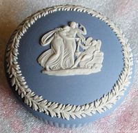 Top view of jar lid showing white classical figures in relief and the leaf garland border on blue jasperware.