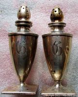 Two urn-shaped sterling silver shakers showing monogram “G” on fronts.