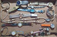Overview of the 16 watches alongside the watch necklace and matching bracelet, displayed in a box showing various band types and watch face designs.