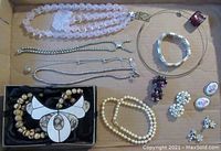 Overview of multiple jewelry pieces including necklaces, bracelets, earrings, and rings laid flat in box.