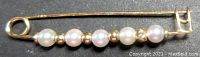 Full view of the 14K gold safety pin style brooch decorated with six cultured pearls separated by gold beads.