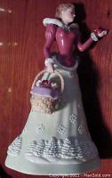 Full view of Lenox 2013 Christmas Princess Colette figurine showing front view with cardinal on hand and basket of Christmas items in the other hand, with snowflake detail on skirt.