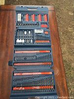 Fold-out Ryobi plastic case fully open showing all compartments with drill bits and screwdriver bits arranged inside, some slots empty.