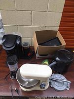 Kitchen appliances and accessories on wooden table against beige wall.