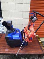 Blue Snow Joe electric snow blower showing side profile with orange extension cord wrapped on handle.