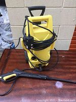 Front view of yellow Karcher electric pressure washer unit on wooden surface with black and yellow spray gun placed in front.