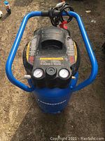 Top-down view of Mastercraft air compressor showing black control panel with two pressure gauges and control knob, blue handle bars, and power cable.
