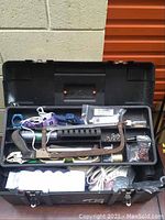 Open black plastic toolbox showing various hand tools inside such as a hand saw, wrenches, and c-clamp.