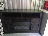 Full frontal view of TV stand showing open shelf, two side cabinet doors, and chimney insert with decorative logs visible