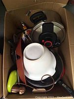 Top view of box showing various kitchen items including pots, pans, a white bowl, spatulas, and utensils packed together