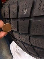 Close up of tire tread with coin for depth measurement.