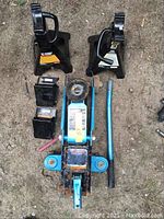 Top view of the 5-piece tire changing set featuring the blue hydraulic floor jack, 2 black jack stands and 2 black wheel chocks on dirt ground.