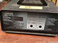 Front view of black Eliminator Intelligent Battery Charger with digital display and control panel showing charging modes and indicators.