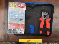Plastic organizer box with compartments holding assorted electrical terminals in various colors beside a pair of orange and black pouch pliers in a black pouch.