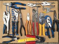Top view of assorted pliers, locking pliers, crimping, and cutting tools laid out on cardboard for sale.