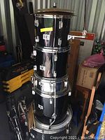 Photo of stacked black SWB drum shells including bass drum, floor tom, mounted toms, and snare with drumsticks placed on bass drum.