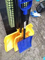 Three snow shovels grouped together showing yellow and blue plastic blades and black shafts with D-grip handles.