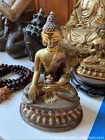 Brass-tone seated Buddha statue on lotus base and smaller Buddha on wooden pedestal seen together