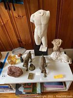 Overview photo of lot showing male torso sculpture, metal animal figurines, small carved bust, carved animal figure, reddish rock, and Zippo lighter.