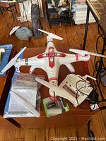 Photo showing the Supernova Soy quadcopter drone on a table. Included remote controller, spare propeller, charger and instruction manual.