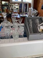 Overview of the decanter, cut glassware including tumblers and cordial glass, and the boxed champagne flutes on a counter.