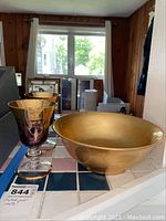Large decorative gold bowl and two blue glasses with gold decoration on tiled table in natural light.