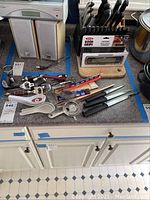 Wide view of knife set in block, assortment of bottle openers, strainers, and kitchen utensils on counter