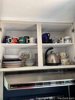 Image showing a kitchen cabinet with mugs on the top shelf, plates and bowls on lower shelves, and an electric kettle.