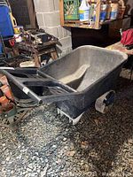 Side angled view of black plastic wheelbarrow showing basin, wheel, and handles in basement setting.
