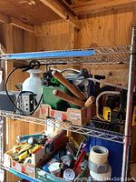 Metal shelving unit inside shed with various tools and gardening equipment, including spray bottle, hand pruners, and rolls of tape, showing storage arrangement of the lot.