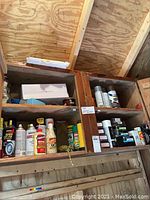 Wide view of wooden shelf containing assorted spray paints, wood glue and hardware