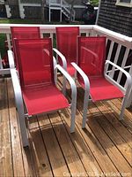 Four red mesh seat patio chairs with white metal frames arranged on wooden deck. Frame shows rust and scratches.