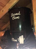 Photo showing black speckled clam steamer pot with white text 'Steamed Clams' on lid and 'Clam Broth' with spigot on pot body.
