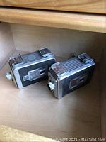 Two Kodak Brownie II 8mm film cameras placed side by side inside a wooden drawer, showing front and side details.