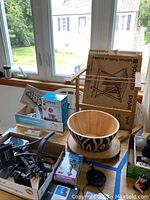 Photo showing large wooden bowl with black hand-painted design, grinder and boxed items around it on table by window