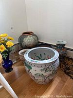 Photo of the ceramic planters including one with floral motif and one with shell-like textured design, plus visible smaller pots and vase