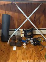 Photo of four dumbbells (two 5 lb. pairs, two 20 lb.), rolled black yoga mat, resistance bands in bag, hand squeezer, water bottle, and athletic tape on wooden floor with white metal frame stand.