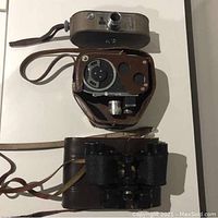 Top view of the old cameras and binoculars showing the Keystone Pathfinder K-29, the film camera in leather case, and binoculars.