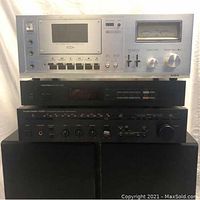 Stack of stereo components: Aiwa cassette deck on top, Proton tuner below, Harman Kardon receiver below that, with ESM-2 speakers under them
