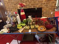 Photo showing various decorative items including red and clear vases, ornate metal candlesticks, votive candle holders with red candles and stones, decorative fans, and green ceramic pieces arranged on a folding table.
