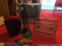 Full view of fireplace tools set, trash bin, magazine rack, and handheld blower on red carpet