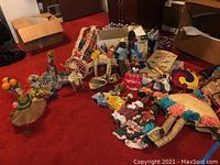 Wide angled photo showing the entire collection of Caribbean straw dolls, fabric dolls, handheld woven fans, miniature woven furniture, and other souvenirs spread on a red carpet.
