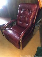 Vintage burgundy leather recliner chair angled front view showing padded seat, button-tufted backrest, and metal side panels.